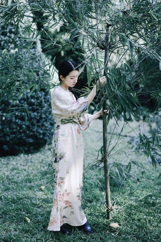 一位穿着传统服装的年轻女子在花园里拿着一棵树。