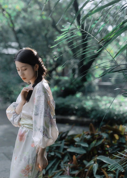 一位穿着日本传统和服的年轻女子站在花园里 在伞下。