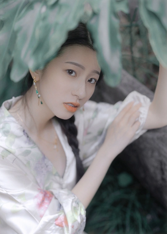 一位穿着白色连衣裙的年轻女子在树前摆姿势