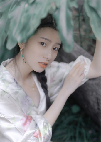 一位穿着白色连衣裙的年轻女子在树前摆姿势