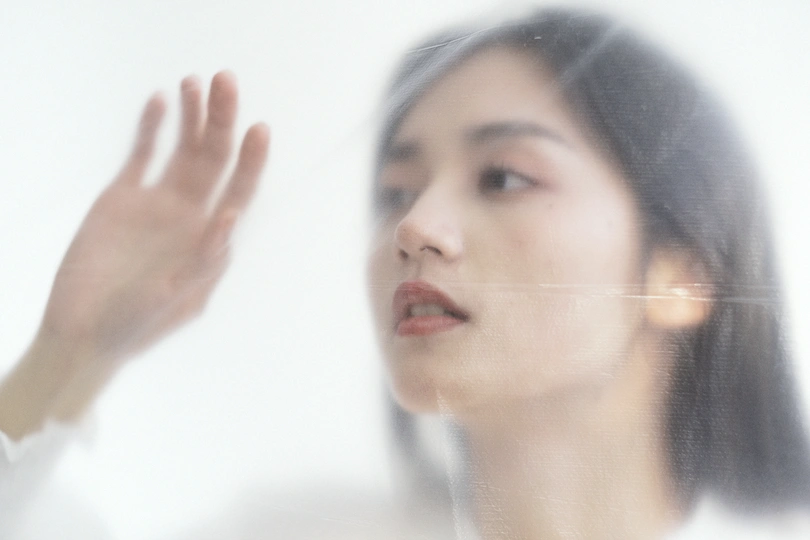 一位年轻女子透过镜子的玻璃看自己的脸