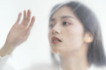 一位年轻女子透过镜子的玻璃看自己的脸