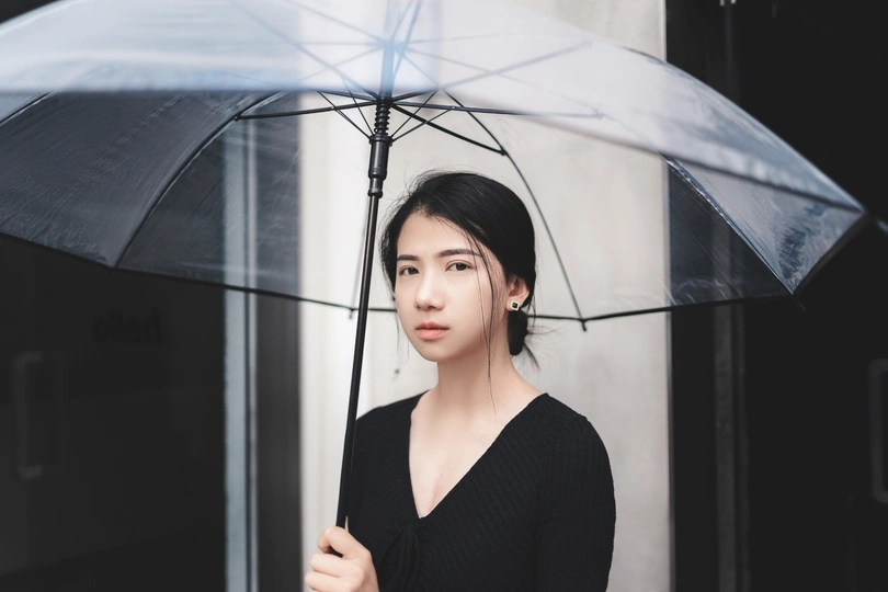 一个穿着黑色连衣裙的年轻女子拿着一把透明的雨伞