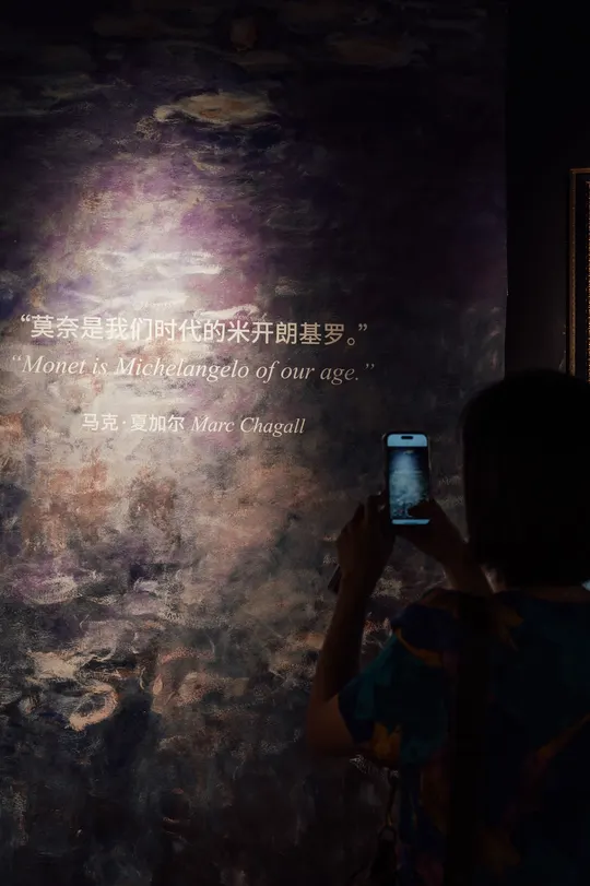 一个年轻女子站在一个光线昏暗的房间里 正在看她手机上的图片。