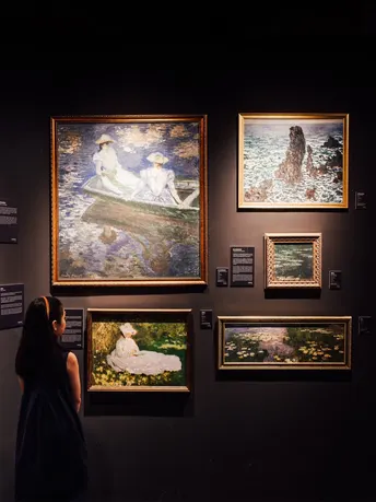 一个女性站在艺术画廊里 正在看墙上的画。