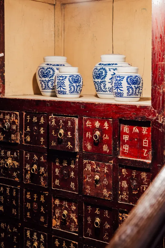 一个带有木质抽屉的房间 书架上有书和蓝白花瓶。