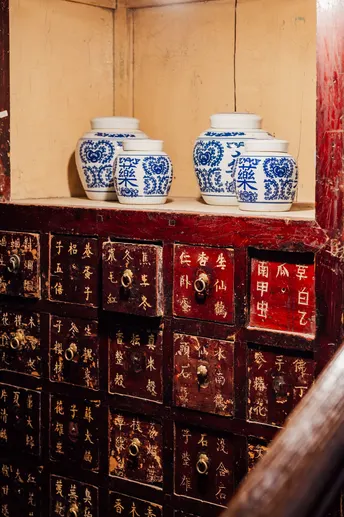 一个带有木质抽屉的房间 书架上有书和蓝白花瓶。