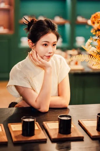 一个年轻女子坐在桌子旁 桌子上放着寿司、蜡烛和花。