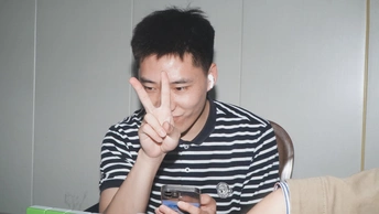 一个年轻人坐在桌子旁 手里拿着笔记本电脑 用手指按在脸上 手心向上 正在看他的手机。