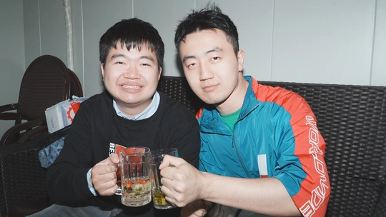 一个年轻男子拿着啤酒坐在另一名年轻男子旁边的沙发上 为拍照做姿势。