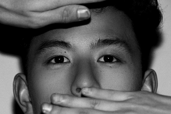 一个黑头发遮住眼睛的年轻人看着镜头 把手放在脸上