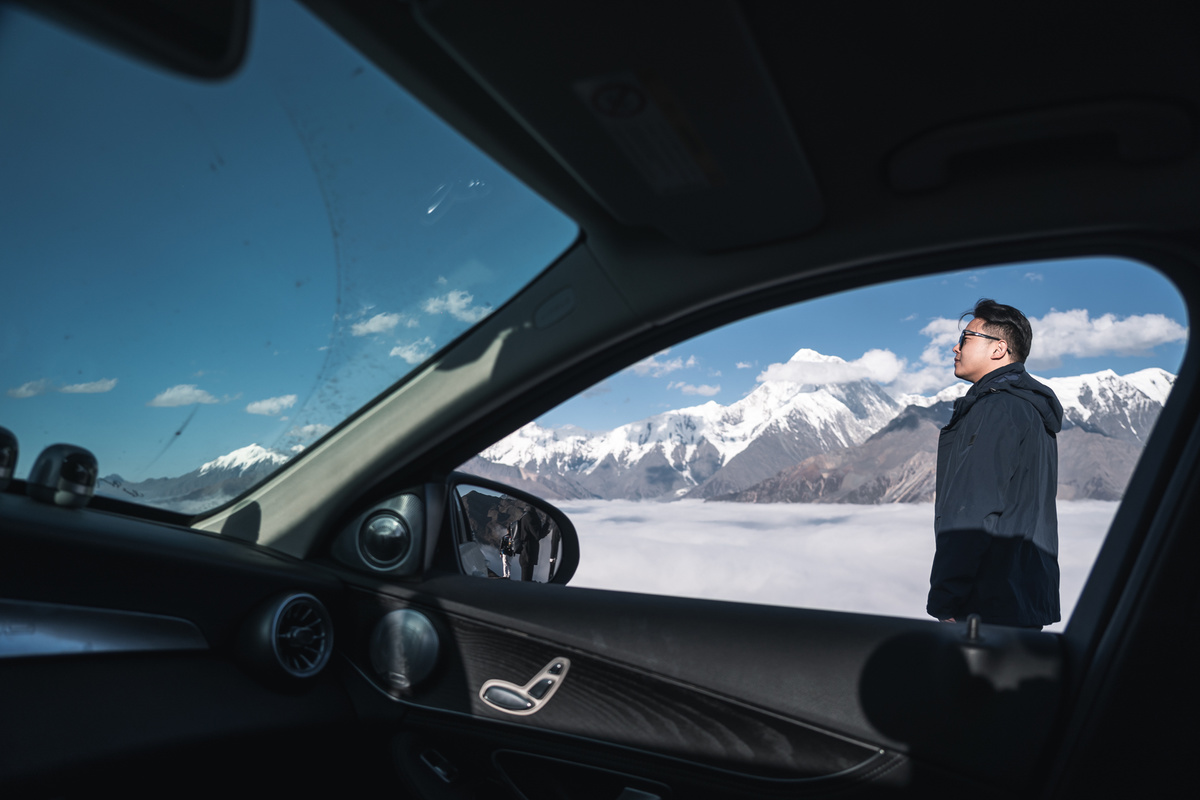 一位男士正在汽车窗口凝视着被雪覆盖的山脉。