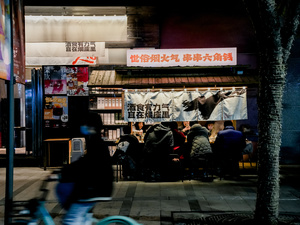 一个人骑着蓝色的自行车在夜晚的街道上 街道两侧有商店和人。