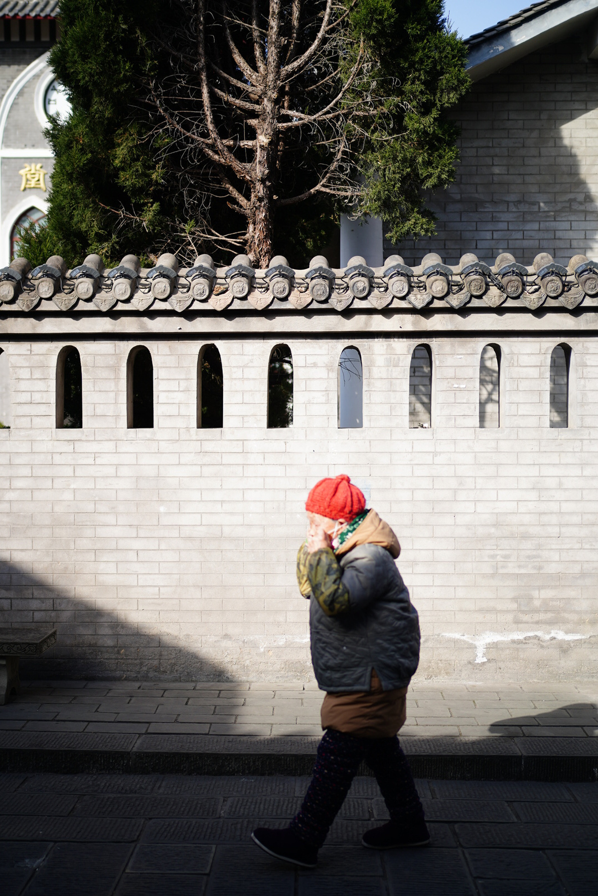 一位戴红帽子的女人走在一条街旁边的一堵墙下