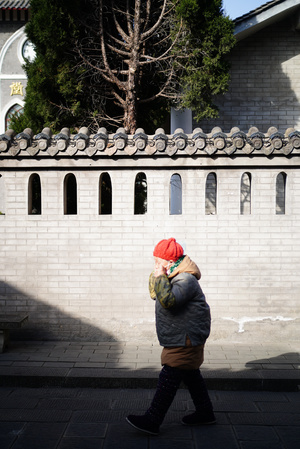 一位戴红帽子的女人走在一条街旁边的一堵墙下