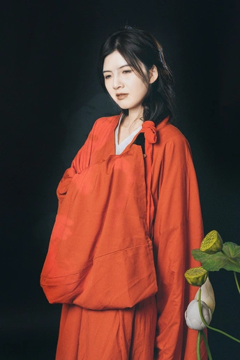 一位穿着橙色连衣裙的年轻女子站在一束白色花的前面 而一位穿着橙色衬衫的年轻男子站在她身后。
