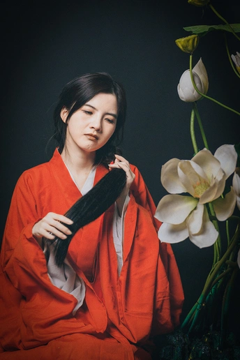 一位穿着红色长袍的年轻女子手持一束白色花朵摆姿势