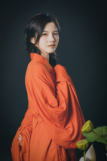 一位穿着橙色长袍的年轻女子正在为一幅肖像画站在一束花旁边。