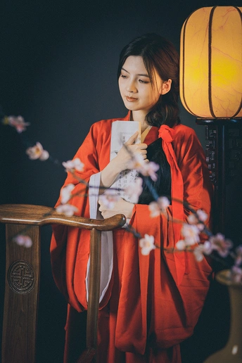 一位穿着红裙子的年轻女子在灯前和一张有花桌的桌子前摆姿势