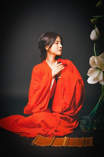 一位穿着红衣服的女人坐在一个插满白色花朵的花瓶旁边。
