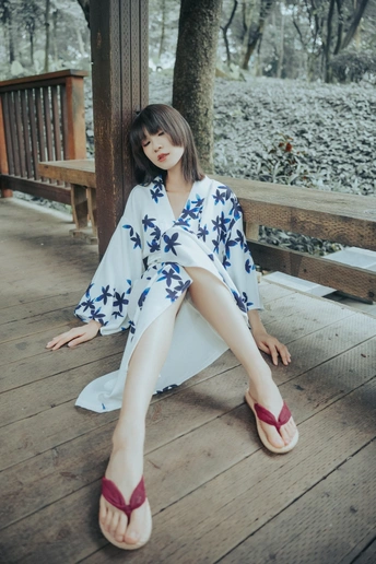 一个穿着和服和红鞋子的年轻女人坐在门廊的木长椅上