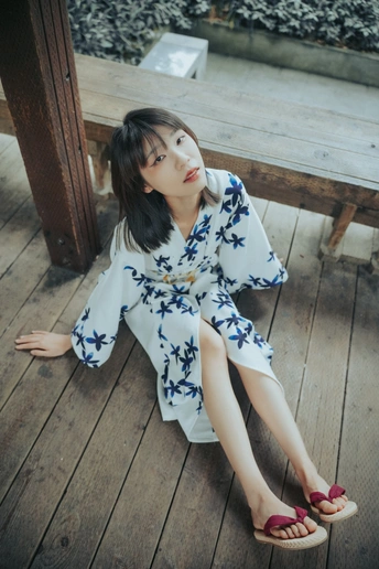 一位身穿蓝白相间连衣裙的年轻女子坐在甲板上的木长椅上 没有穿鞋