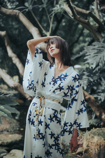 一个穿着白色长袍和蓝色碎花连衣裙的模特站在森林里