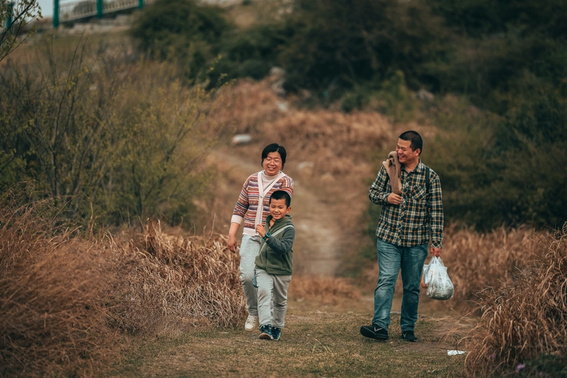 一个小男孩和一个男人背着袋子走在小路上 几个人在后面走