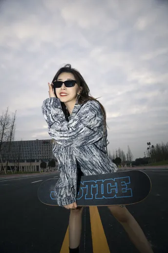 一位年轻女子站在公路中央 手里拿着滑板。
