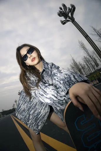 一个戴太阳镜的年轻女子站在公路中央 手里拿着滑板。