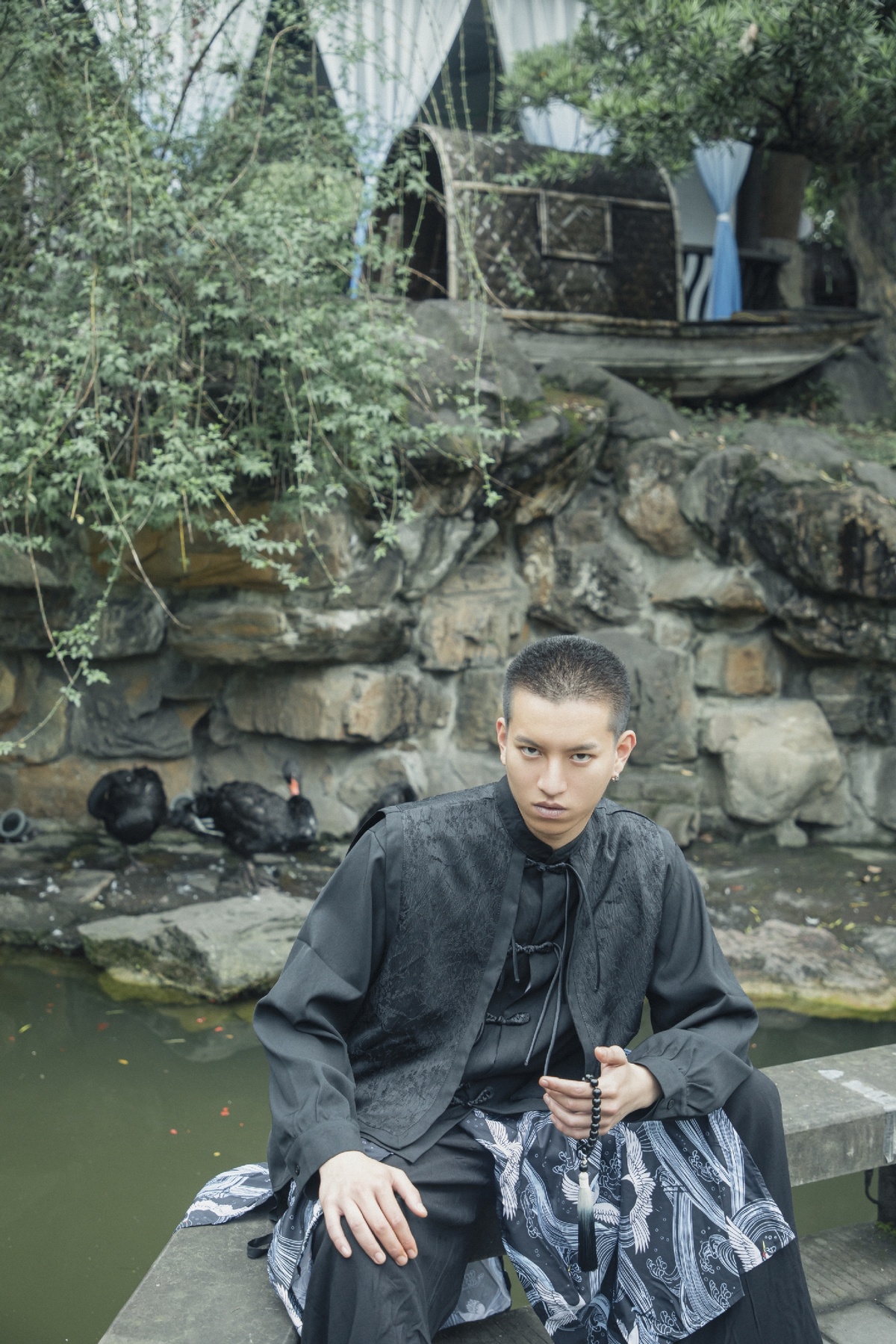 一位年轻男子坐在池塘前的岩石上 背景中有瀑布和水潭。