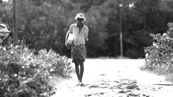 一个老人和女人在泥土路上行走 带着一把伞。