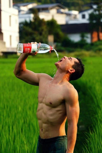 一位年轻人正在绿地上喝水。