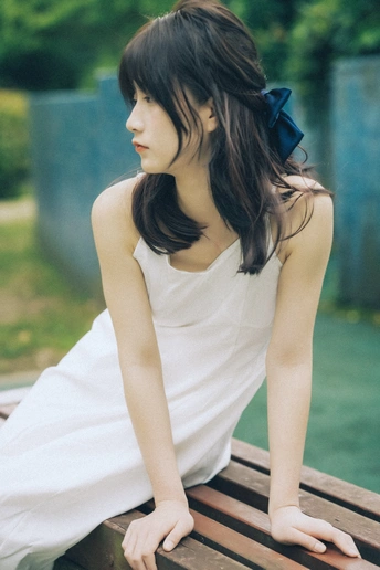 一位蓝头发、身穿白色连衣裙的年轻女子坐在木长椅上