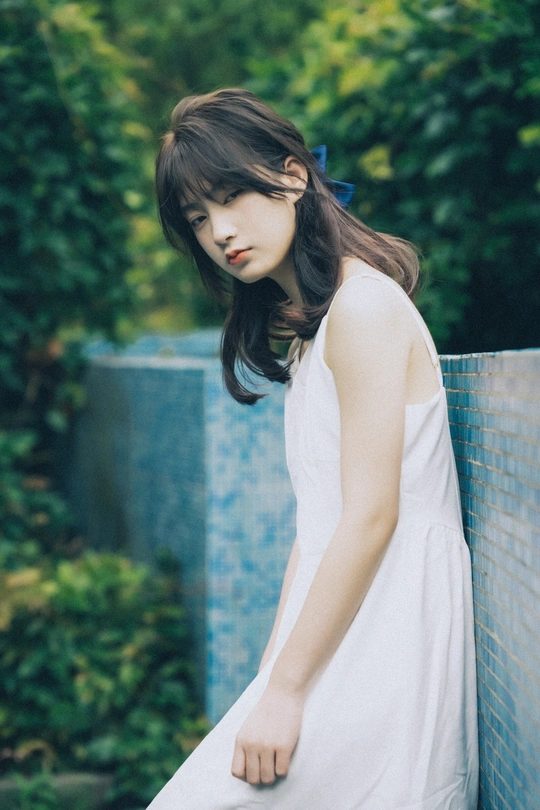 一个穿着白色连衣裙靠在蓝色栅栏上的年轻女子