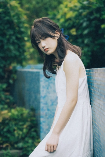 一个穿着白色连衣裙靠在蓝色栅栏上的年轻女子