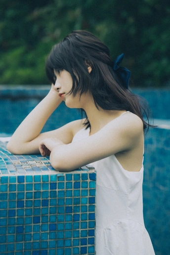 一个穿着白色连衣裙的年轻女子靠在蓝色的喷泉旁