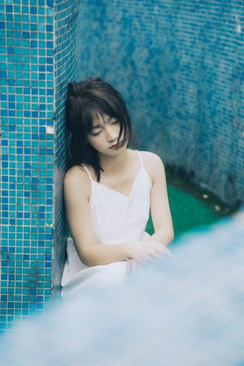 一位身穿白色衣服的年轻女子坐在蓝色的池边