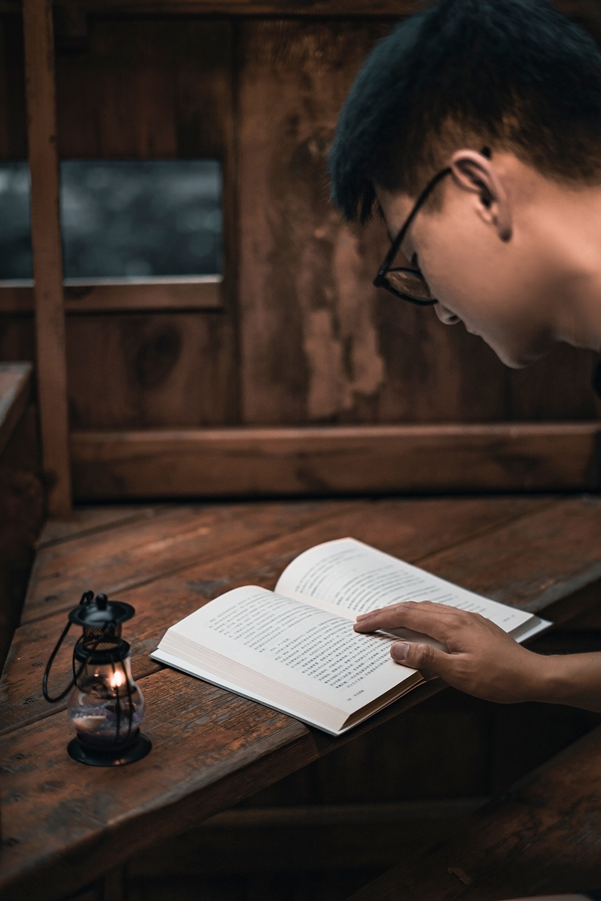 一个戴着眼镜的年轻人在一个有灯笼和灯的木屋里看书