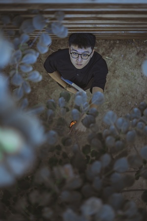 一个戴眼镜的年轻人站在一丛花丛旁