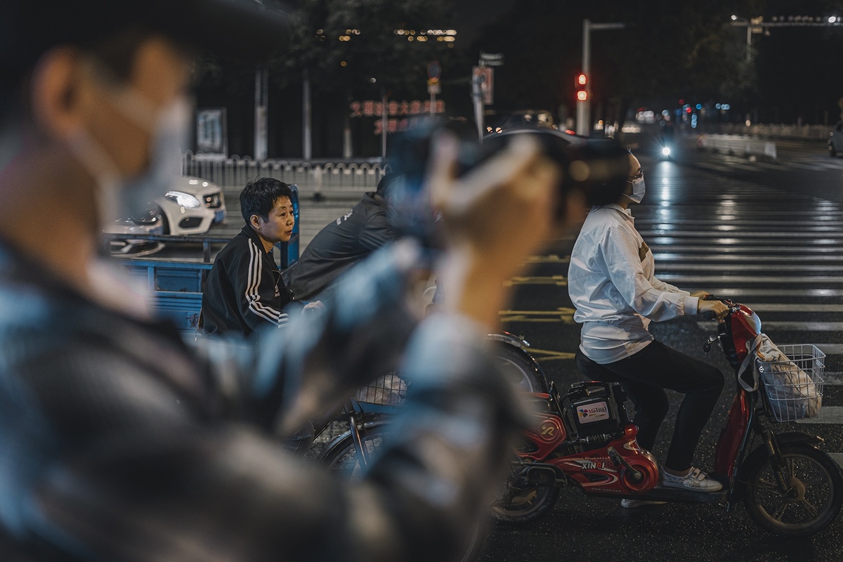 一名戴着口罩的男子晚上在街上骑着摩托车 行人横穿马路 一名男子骑着摩托车
