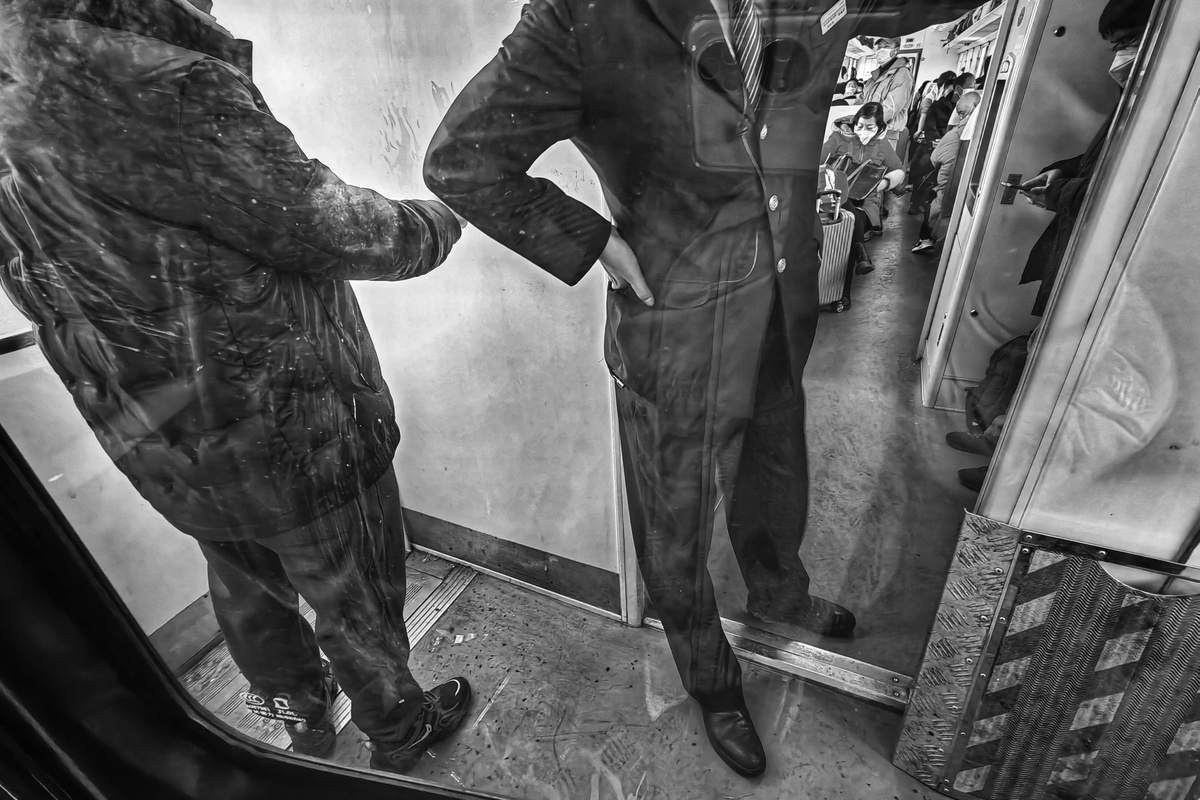 一张黑白照片 一个穿西装的男人站在地铁边的镜子里。