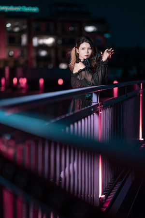 一位年轻女子站在夜晚的桥上 背景中有围栏和灯光。