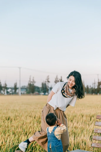 一个年轻女子坐在麦田里的长凳上 小女孩在空中跳跃。
