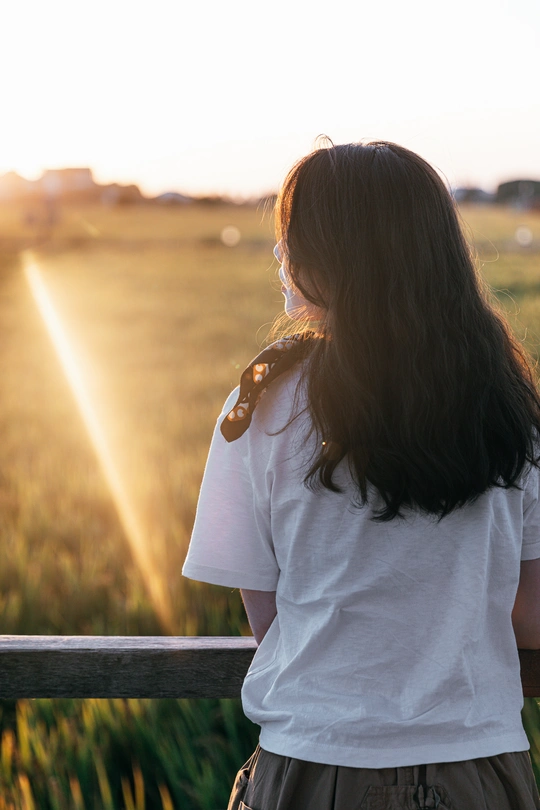 一位年轻女子在日落时分站在长凳上 头发随风飘动 眺望着田野。