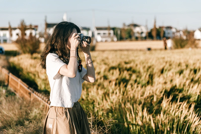 一位年轻女子站在草地上 用相机拍照。
