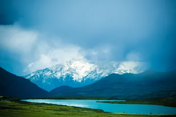 绿色山谷中的一个湖泊 周围有雪山和蓝天。