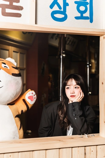 一位年轻女子站在窗前 身后坐着一只毛绒动物