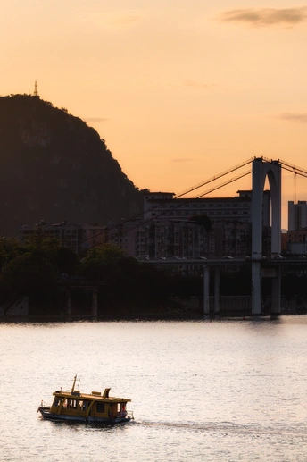 一艘小船在夕阳下漂浮在靠近城市和一座桥的大型水域上。