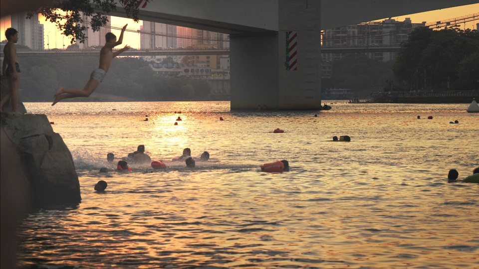 夕阳下在桥附近的水域中游泳的人们